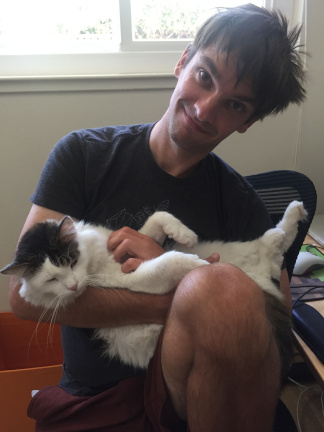 A picture of the author while smiling and holding a cat upside-down